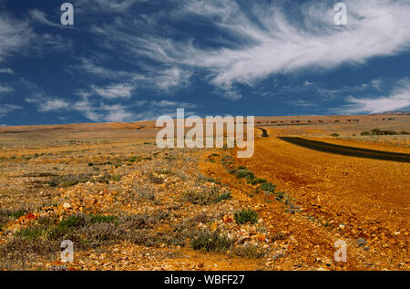 Straße erstreckt sich über riesige rote steinigen kargen Ebenen, zu fernen Horizont unter blauem Himmel strecken im Outback Queensland bei Dürre Stockfoto