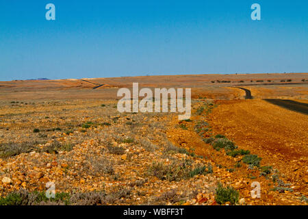 Straße erstreckt sich über riesige rote steinigen kargen Ebenen, zu fernen Horizont unter blauem Himmel strecken im Outback Queensland bei Dürre Stockfoto