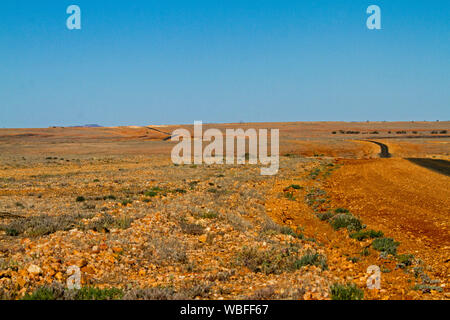 Straße erstreckt sich über riesige rote steinigen kargen Ebenen, zu fernen Horizont unter blauem Himmel strecken im Outback Queensland bei Dürre Stockfoto