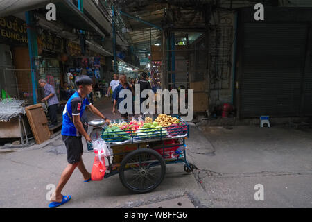 Am frühen Morgen, in der Frühe kommerzielle Aktivität, eine mobile Anbieter drückt seine Frucht Warenkorb durch Sampeng Lane in Chinatown, Bangkok, Thailand Stockfoto