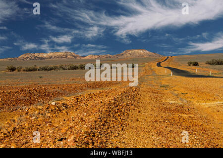 Straße ausdehnend über steinigen kargen Ebenen, die fernen Hügel und Horizont unter blauem Himmel strecken im Outback Queensland bei Dürre Stockfoto