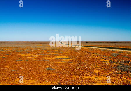 Straße erstreckt sich über riesige rote steinigen kargen Ebenen, zu fernen Horizont unter blauem Himmel strecken im Outback Queensland bei Dürre Stockfoto