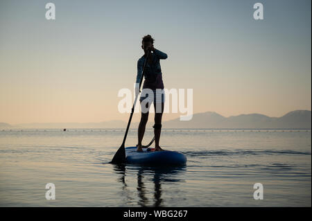 Junge Frau paddeln auf einem Stand Up Paddling Board auf einem ruhigen Morgen Meer Stockfoto