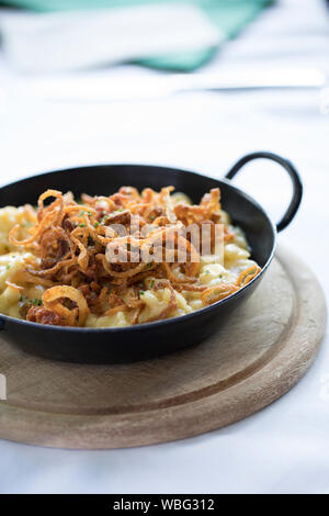 Traditionelle alpenländische Käse Teller in eine eiserne Pfanne auf einem Holzbrett serviert. Stockfoto