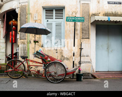 Einen alten klapprigen Trishaw cab auf dem Gehweg von einem verfallenen Gebäude in Penang, Malaysia geparkt. Stockfoto