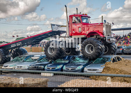 Die Big Pete Monster truck Zerkleinerung ein Stapel von Schrott Autos ziehen und Ihre maßgeschneiderte Trailer während einer Demonstration an einem Monster Truck Show Stockfoto