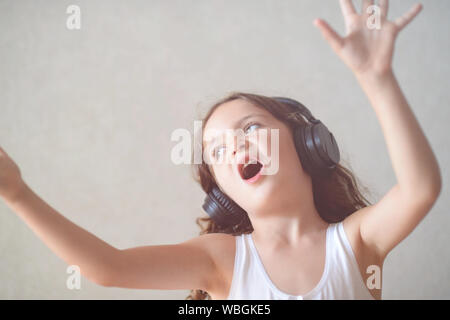 Kleine kaukasische Mädchen in schwarz Kopfhörer singen Song winkende Hände innen aufgeregt Stockfoto