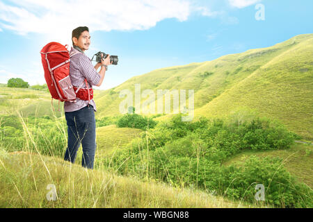 Asiatischer Mann mit einem Rucksack mit einer Kamera Bilder auf den grünen Hügeln zu nehmen Stockfoto