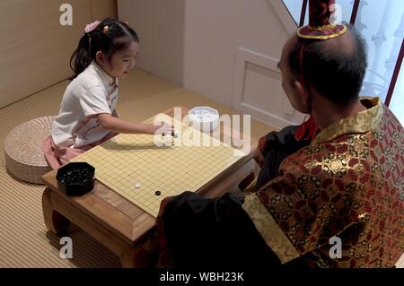 (190827) - ZHENGZHOU, Aug 27, 2019 (Xinhua) - ein Kind spielt (weiqi) Spiel mit einer freiwilligen tragen traditionelle constume während der Chinesischen Sport Heritage Ausstellung in Zhengzhou Museum in Zhengzhou, Hauptstadt der zentralchinesischen Provinz Henan, Aug 26., 2019. Über 175 Exponate wurden auf dem Display während der Ausstellung, die aus hier Montag trat. (Xinhua/Li an) Stockfoto