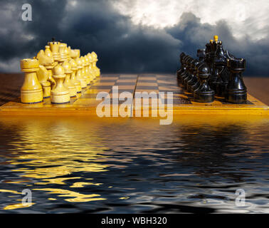 Schachfiguren bereit, auf Schachbrett, auf dunklen Wolken Hintergrund und mit Reflexion im Wasser zu spielen Stockfoto