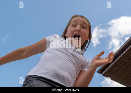 Extrem glücklich kleines Mädchen springt mit rised Hände und öffnete den Mund. Mädchen 9 Jahre alt Springen auf einem Trampolin. Zurück zu Schule. Stockfoto