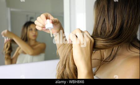 Junge Frau mit unter Druck stehendem Öl Maske mit Haar Tipps vor einem Spiegel. Haarpflege Konzept. Fokus auf das Haar. Stockfoto