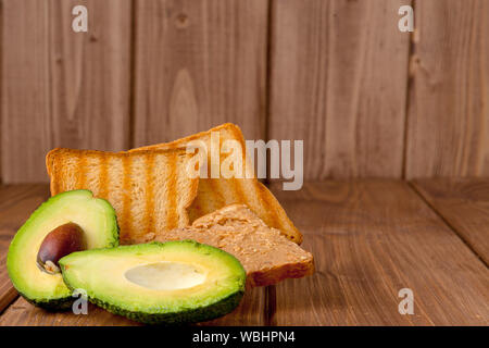 Avocados und Toaster mit Erdnuß-Paste auf einem hölzernen Hintergrund. Hausgemachten köstlichen und gesunden Frühstück Toast. Stockfoto