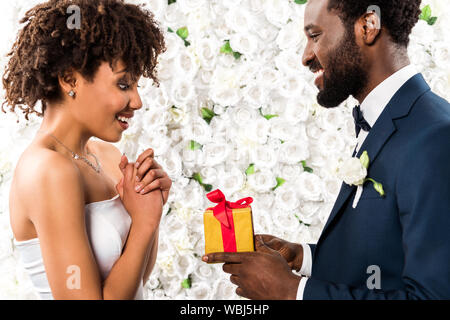 Happy afrikanischen amerikanischen Mann, der Gegenwart zu überrascht Braut in der Nähe von Blumen Stockfoto