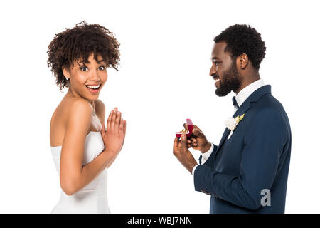 Fröhliche african american man Holding Box mit Ring und macht Vorschlag überrascht, Frau isoliert auf weiss Stockfoto