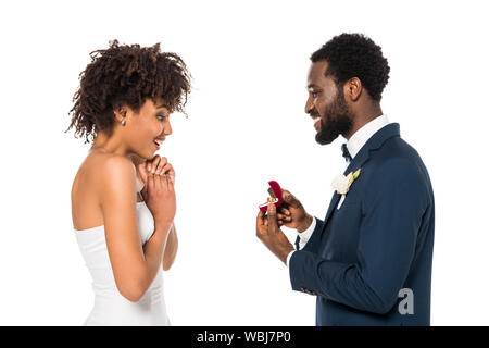 African American man Holding Box mit Ring und macht Vorschlag überrascht, Frau isoliert auf weiss Stockfoto