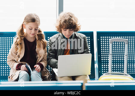 Kinder auf der Suche nach Laptop und sitzen auf blauen Sitze in der Wartehalle im Flughafen Stockfoto