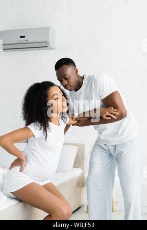 African American man hilft, schwangere Frau, stehend aus dem Bett Stockfoto