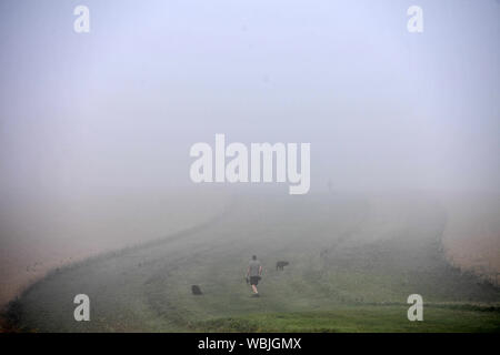 Ein Mann seine Hunde durch eine Schicht Morgennebel in Chesterton, Warwickshire, nach dem heißesten August Bank Holiday Montag auf Aufzeichnung, mit Temperaturen 33,2 C. Trotz der Nebel, die hitzewelle wird eingestellt, die für einige Teile des Vereinigten Königreichs nach dem rekordverdächtigen Bank urlaub Wetter, um fortzufahren. Stockfoto