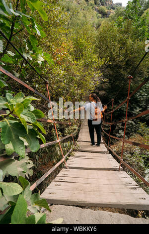 Blick auf eine Frau mit einem Leder Rucksack überqueren eine Hängebrücke in den Wald. Stockfoto