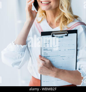 7/8-Ansicht von Frau sprechen auf Smartphone und Holding Zwischenablage mit Buchstaben fortsetzen Stockfoto