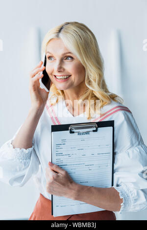 Gerne blonde Frau sprechen auf Smartphone und Holding Zwischenablage mit Buchstaben fortsetzen Stockfoto