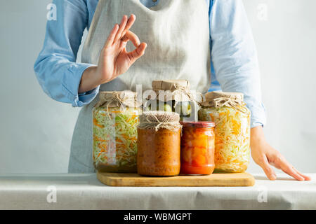 Fermentierte oder eingemachtes Gemüse, verschiedene in Töpfen stehen auf dem Salz vor dem Hintergrund einer Frau in einer Schürze. Die Verarbeitung der Ernte im Herbst. Natu Stockfoto