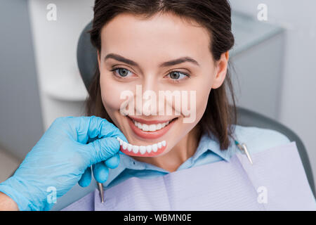 7/8-Ansicht von Zahnarzt holding Prothese in der Nähe von Happy girl in der zahnmedizinischen Klinik Stockfoto