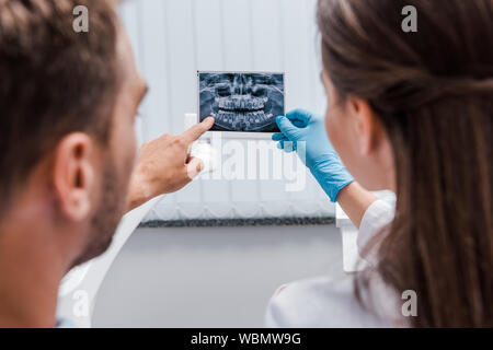 7/8-Ansicht von Zahnarzt Holding x-ray in der Nähe von Patienten zeigte mit dem Finger in Klinik Stockfoto