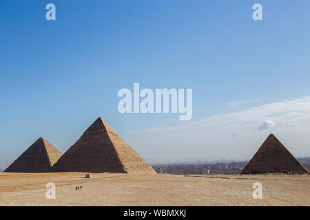 Drei Pyramiden (von links nach rechts) Khufu, Khafre und Menkuare in Ägypten am Morgen mit blauem Himmel. Der Hintergrund ist die Stadt von Gizeh. Drei kleine Stockfoto