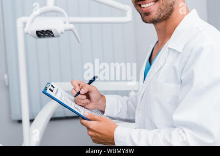 7/8-Ansicht von bärtigen Mann im weißen Mantel der die Feder und die Zwischenablage in der zahnmedizinischen Klinik Stockfoto