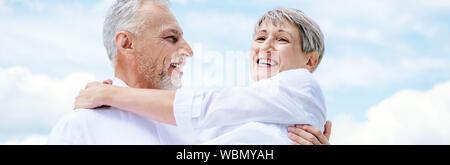Panoramablick von lächelnden älteren Mann anheben Frau unter blauem Himmel Stockfoto