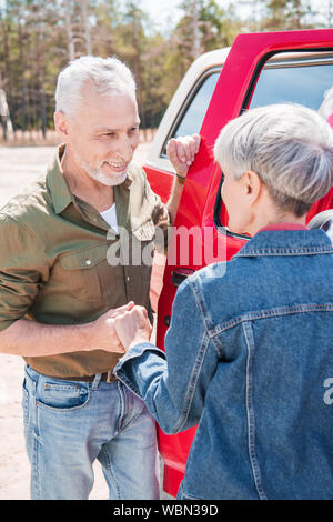 Lächelnd senior Paar in der Nähe von roten Auto, halten sich an den Händen und an jedem anderen Suchen Stockfoto