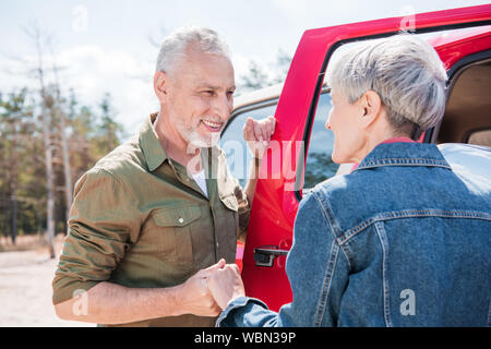 Lächelnd senior Paar in der Nähe von roten Auto, halten sich an den Händen und an jedem anderen Suchen Stockfoto