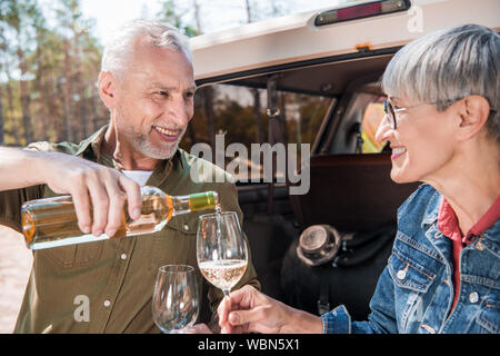 Lächelnd älterer Mann gießen Wein für Wein Gläser und die Frau in der Nähe des Auto Stockfoto