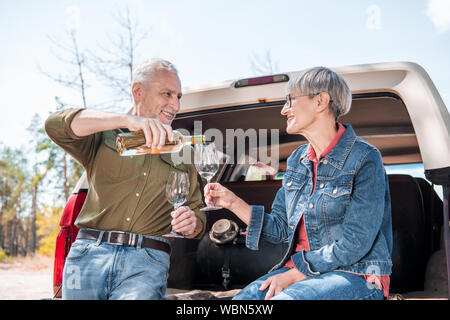 Lächelnd älterer Mann gießen Wein für Wein Gläser und die Frau in der Nähe des Auto Stockfoto