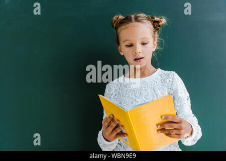 Überrascht Schülerin lesen gelbe Buch auf Grün Stockfoto