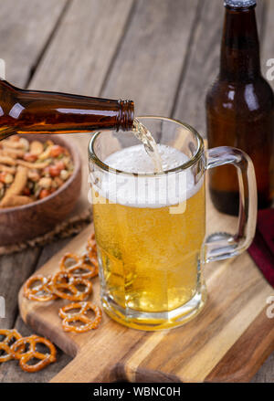 Bier zapfen in ein Glas Becher mit Snacks auf einer hölzernen Oberfläche Stockfoto