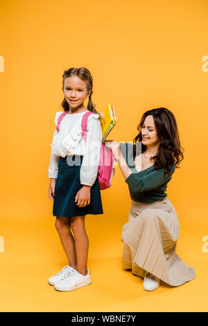 Attraktive Mutter, Bücher im Rucksack von Schulmädchen auf Orange Stockfoto