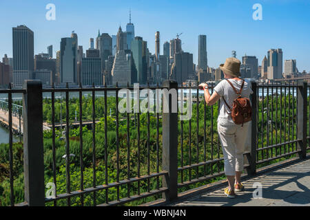 Reife Frau Stadt, Ansicht der Rückseite einer reifen Frau, die auf der Promenade in Brooklyn im Sommer und mit Blick auf die Skyline von Manhattan, New York City, USA Stockfoto