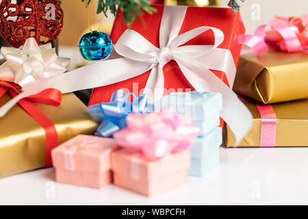 Nahaufnahme einer roten Geschenkverpackung mit einer weißen Schleife unter der Kiefer Baum gesetzt gebunden. Eine blaue kleine Glocke und snowflke hängt am Zweig mit Weihnachtskugeln Stockfoto