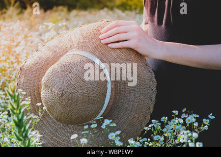 Lieben und Schätzen der Natur. Stroh Hut in weibliche Hände auf ein wunderschönes ländlichen Wiese voller wilder Blumen Stockfoto