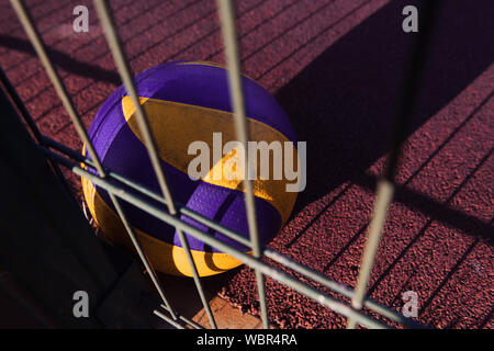 Ein einsamer ball Festlegung auf der roten Erde nach dem Spiel. Volleyball verloren. Sportplatz am Sonnenuntergang mit einem Metallzaun. Stockfoto