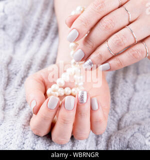 Die gepflegten Frau Hände mit Pastell Nagellack Holding natürliche Perlen, grau gestrickt, Hintergrund, Nahaufnahme Stockfoto