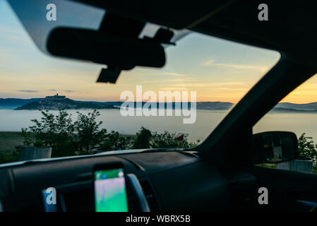 Blick aus dem Inneren des Autos bei Sonnenaufgang in den Bergen Stadt auf dem Gipfel des Hügels Stockfoto