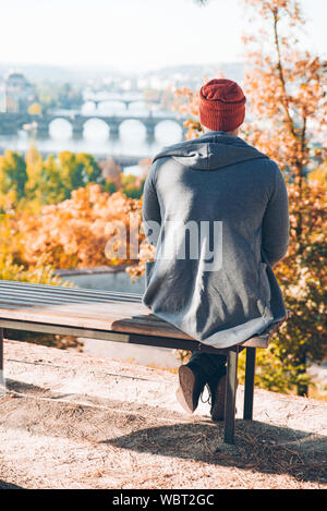 Mann sitzt auf der Bank mit Blick auf den Herbst Prag Stockfoto