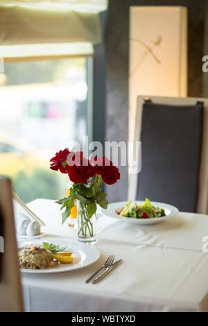 Vertikale selektive Nahaufnahme geschossen roten Rosen auf dem Tisch in der Nähe Teller gefüllt mit Lebensmitteln auf dem Tisch Stockfoto