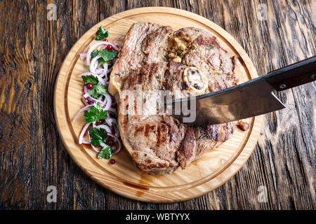 Gekochtes Rindfleisch Steak auf einem runden Schneidebrett. Daneben gehackte Zwiebel und Petersilie ist. In der Nähe der Teig liegt ein Messer Stockfoto