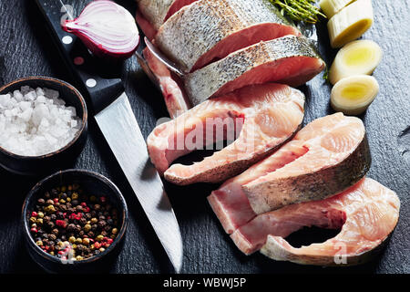 Nahaufnahme der Rohe frische Forellen in Scheiben geschnitten mit Kalk Keile, Lauch, Thymian, Salz und Pfeffer auf einem schwarzen Schiefer Fach auf einem alten rustikalen Holztisch, vie Stockfoto