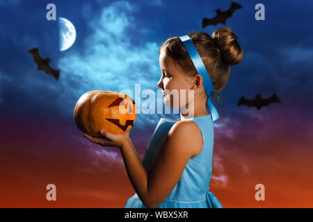 Halloween Feier. Charmantes kleines Mädchen in einem Kostüm der Aschenputtel Prinzessin hält einen Kürbis auf dem Hintergrund der Abend mond Himmel. Stockfoto